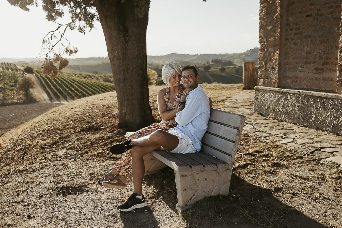 Prewedding da sogno a Nizza Monferrato intorno alla chiesa della Madonna della Neve. Matteo e Fiammetta seduti su di una panchina all'ombra di un grande albero.