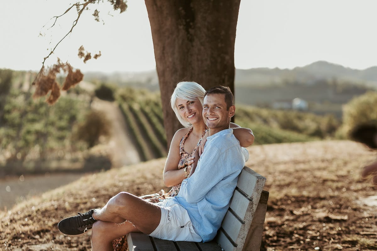 Prewedding da sogno a Nizza Monferrato intorno alla chiesa della Madonna della Neve. Matteo e Fiammetta seduti su di una panchina all'ombra di un grande albero.