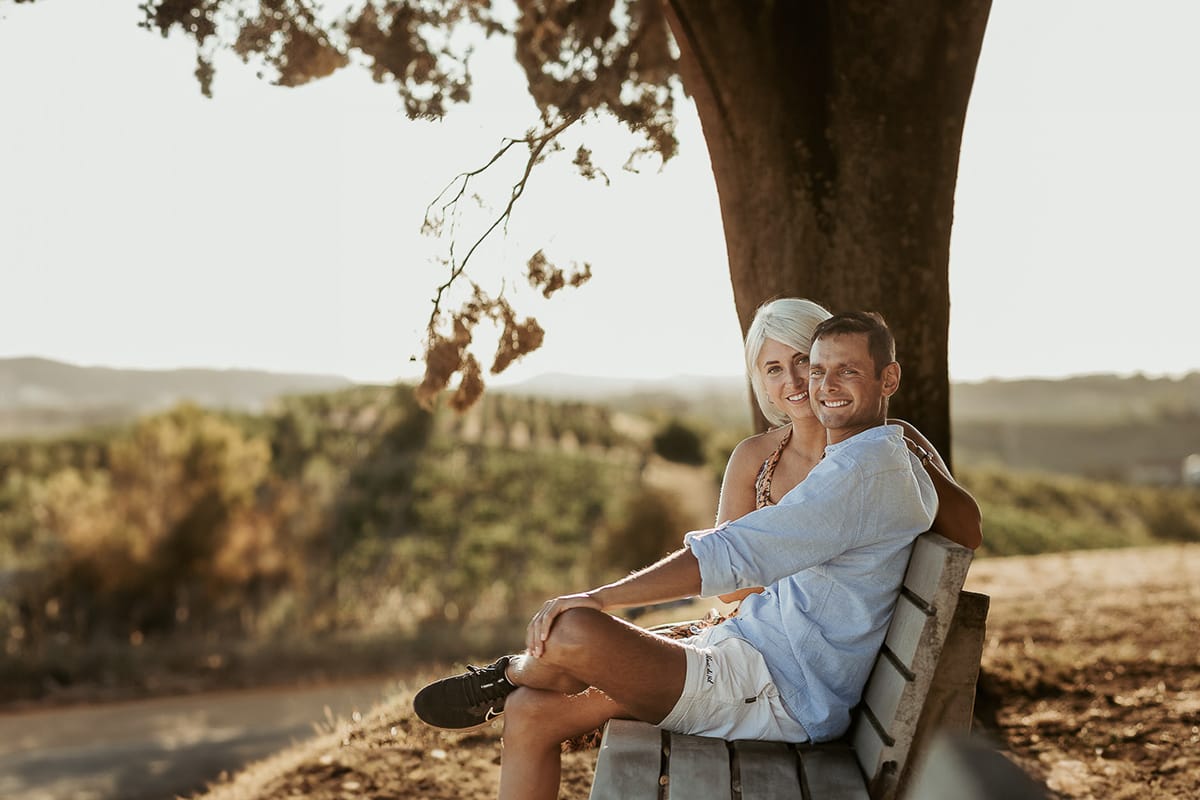Prewedding da sogno a Nizza Monferrato intorno alla chiesa della Madonna della Neve. Matteo e Fiammetta seduti su di una panchina all'ombra di un grande albero.
