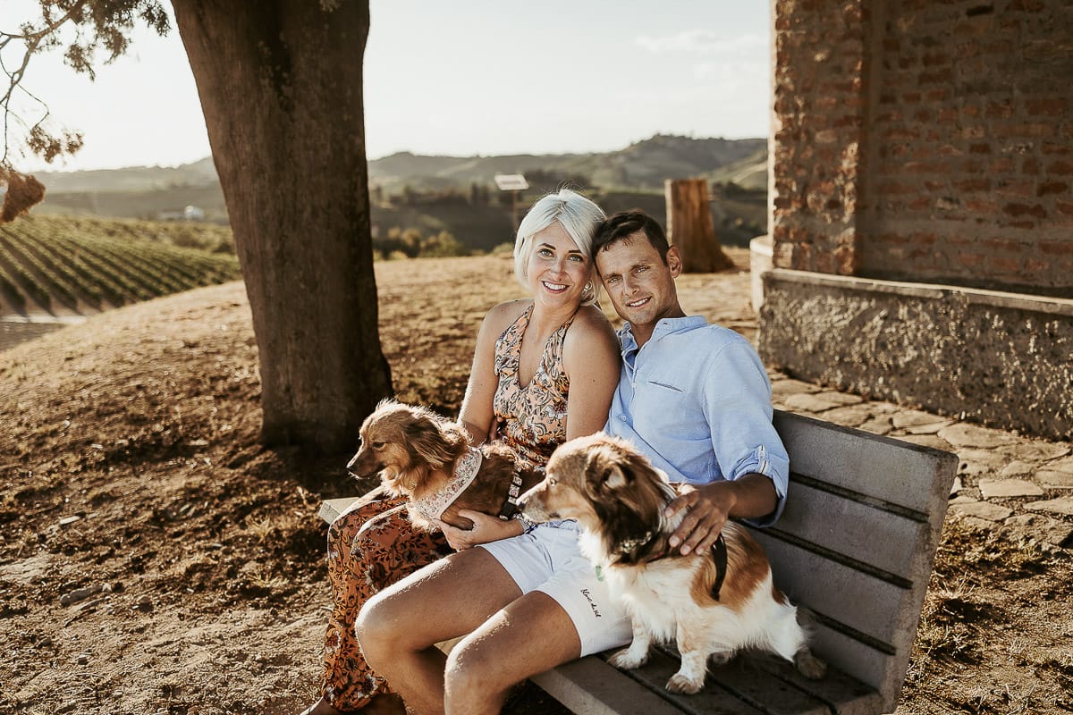 Prewedding da sogno a Nizza Monferrato intorno alla chiesa della Madonna della Neve. Matteo e Fiammetta seduti su di una panchina all'ombra di un grande albero con i volpini Megan e Harry.