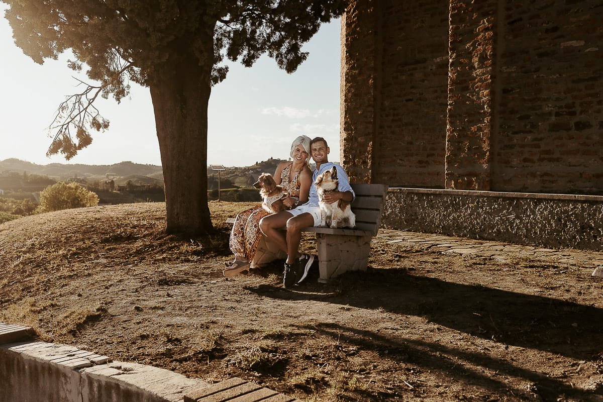 Prewedding da sogno a Nizza Monferrato intorno alla chiesa della Madonna della Neve. Matteo e Fiammetta seduti su di una panchina all'ombra di un grande albero con i volpini Megan e Harry.