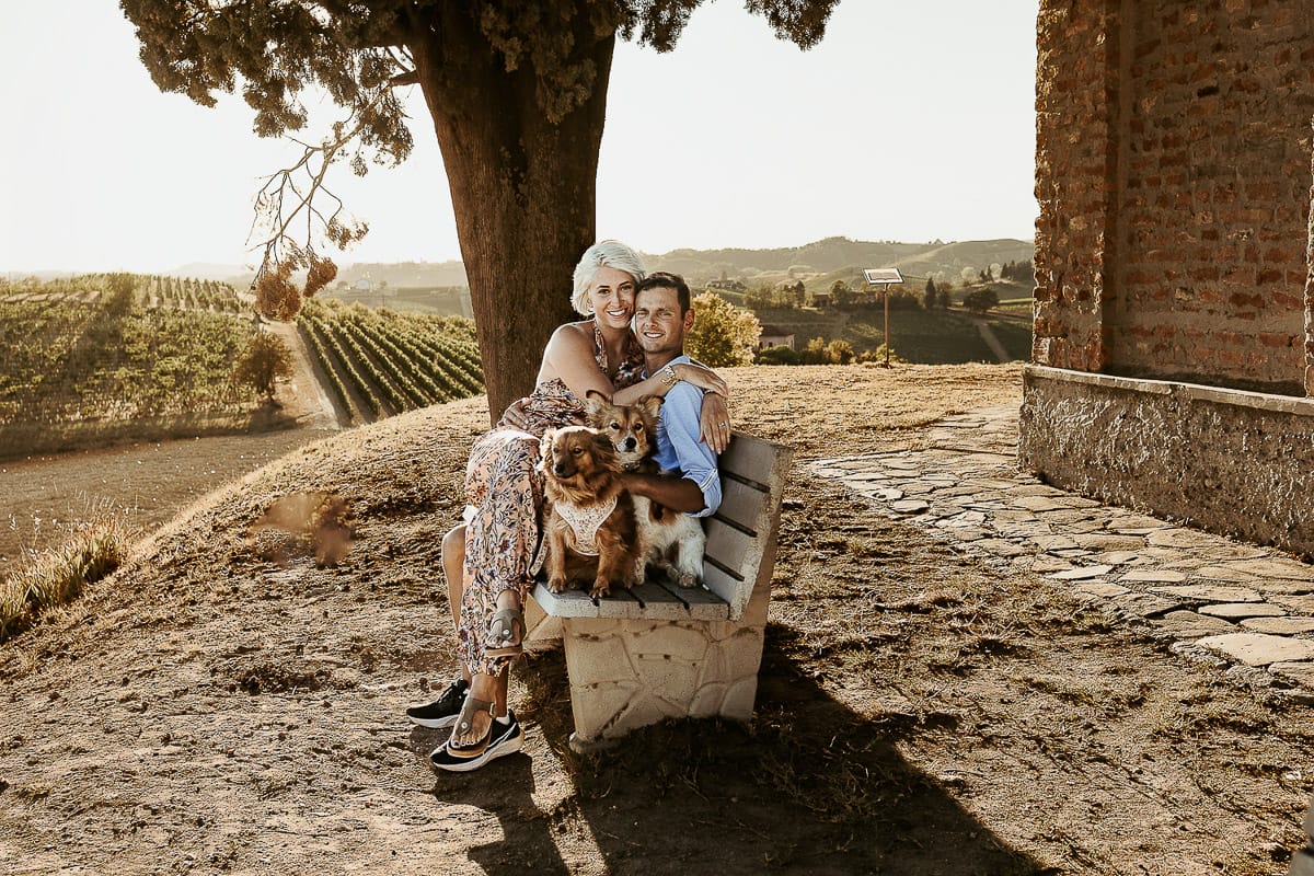 Prewedding da sogno a Nizza Monferrato intorno alla chiesa della Madonna della Neve. Matteo e Fiammetta seduti su di una panchina all'ombra di un grande albero con i volpini Megan e Harry.