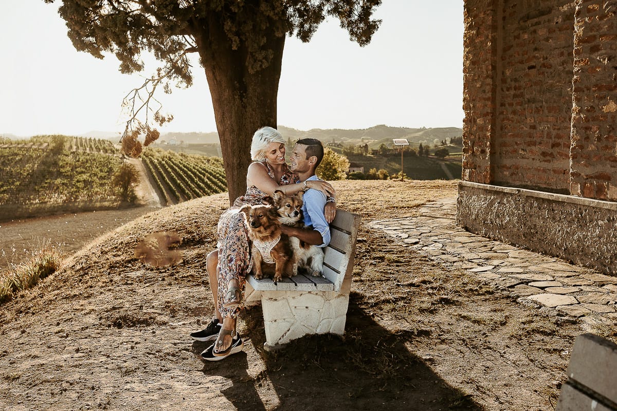 Prewedding da sogno a Nizza Monferrato intorno alla chiesa della Madonna della Neve. Matteo e Fiammetta seduti su di una panchina all'ombra di un grande albero con i volpini Megan e Harry.