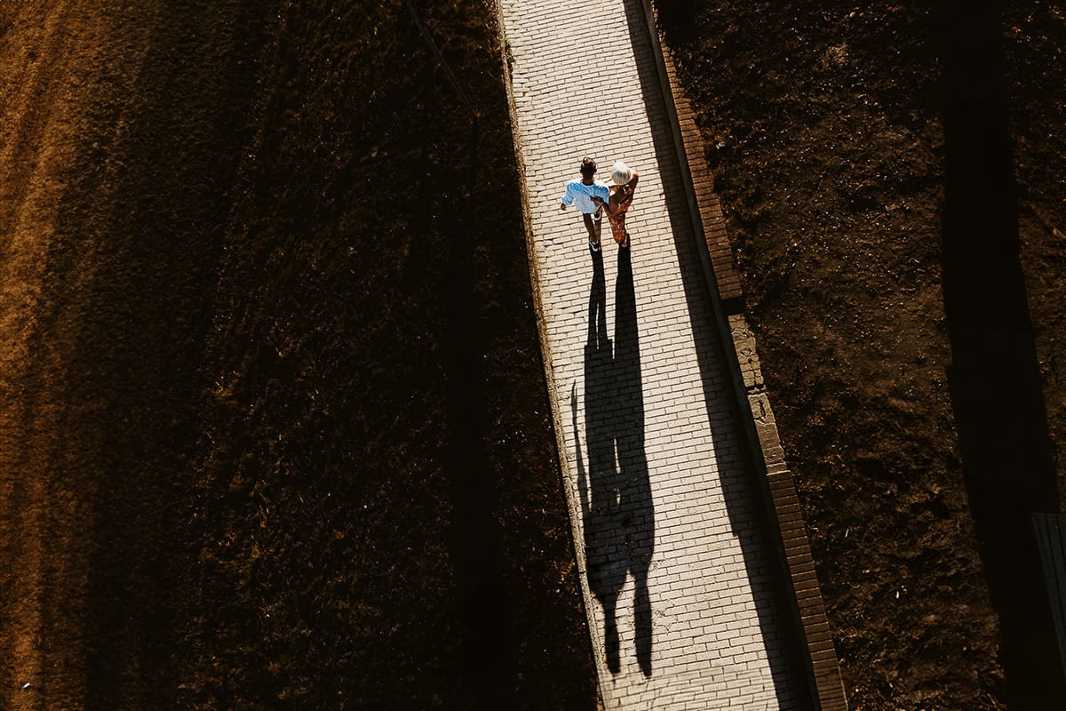 Prewedding da sogno a Nizza Monferrato intorno alla chiesa della Madonna della Neve. Matteo e Fiammetta camminano lungo il vialetto verso i vigneti. Foto aerea dal drone con l'ombra allungata del tramonto