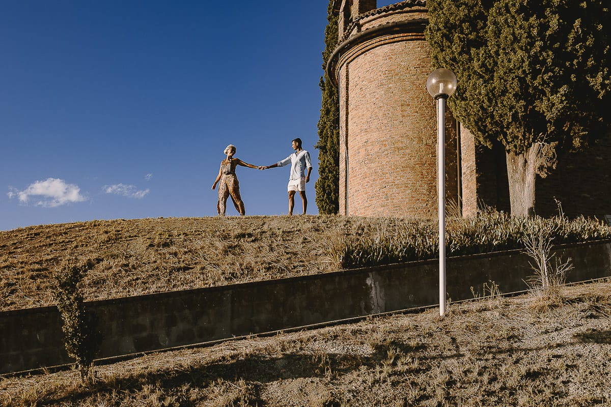 Prewedding da sogno a Nizza Monferrato intorno alla chiesa della Madonna della Neve. Matteo abbraccia Fiammetta. Foto ripresa dal basso. La coppia si staglia nell'azzurro del cielo estivo.