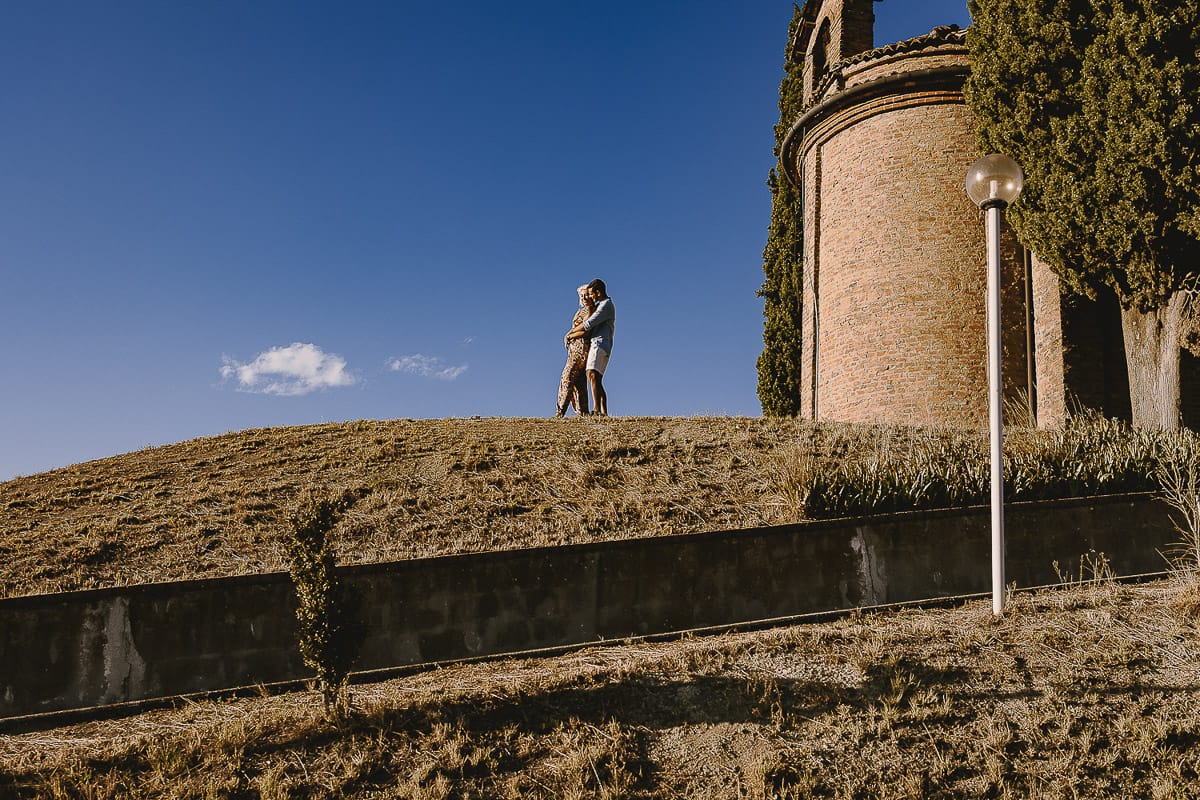 Prewedding da sogno a Nizza Monferrato intorno alla chiesa della Madonna della Neve. Matteo abbraccia Fiammetta. Foto ripresa dal basso. La coppia si staglia nell'azzurro del cielo estivo.