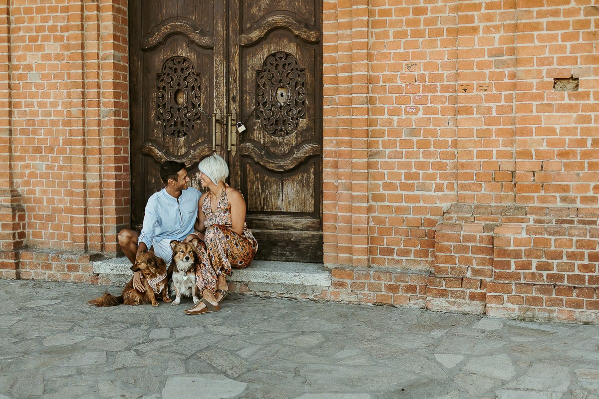 Prewedding da sogno a Nizza Monferrato intorno alla chiesa della Madonna della Neve. Fiammetta e Matteo seduti sul gradino del portone della chiesa con i loro volpini Megan e Harry