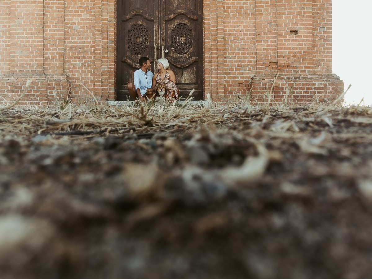Prewedding da sogno a Nizza Monferrato intorno alla chiesa della Madonna della Neve. Fiammetta e Matteo seduti sul gradino del portone della chiesa con i loro volpini Megan e Harry Foto scattata dal drone posto sul terreno.