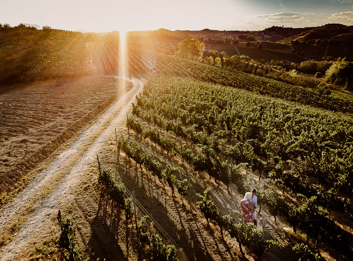 Prewedding da sogno a Nizza Monferrato intorno alla chiesa della Madonna della Neve. Fiammetta e Matteo nel vigneto. Foto aerea dal drone con il flare del sole che sta tramontando.