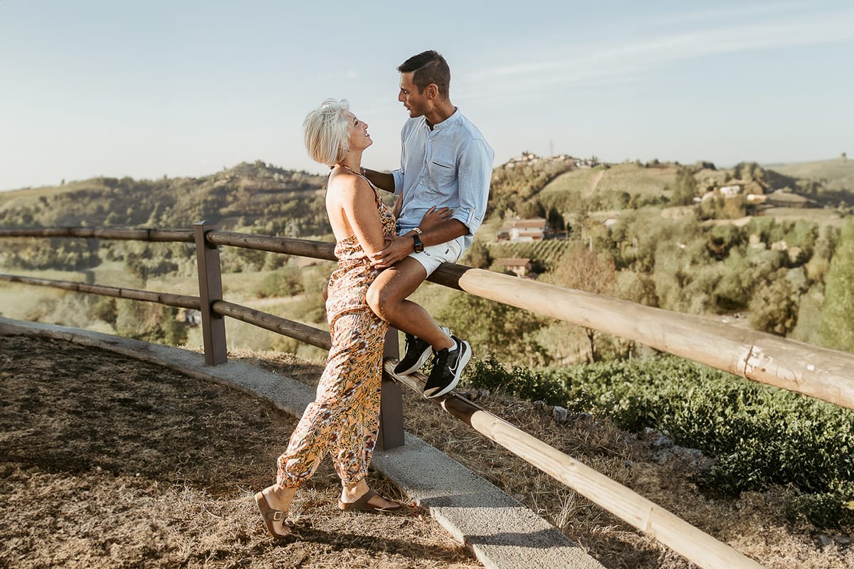 Prewedding da sogno a Nizza Monferrato intorno alla chiesa della Madonna della Neve. Matteo seduto su di una staccionata di legno. Fiammetta lo guarda.