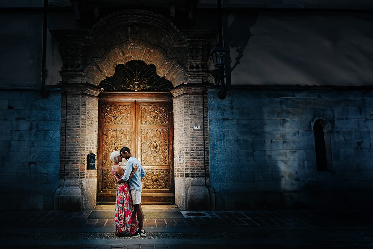 Prewedding da sogno a Nizza Monferrato nel centro storico. Fiammetta e Matteo davanti al bellissimo portone scolpito di un palazzo. storico. Flash off camera puntato verso il portone