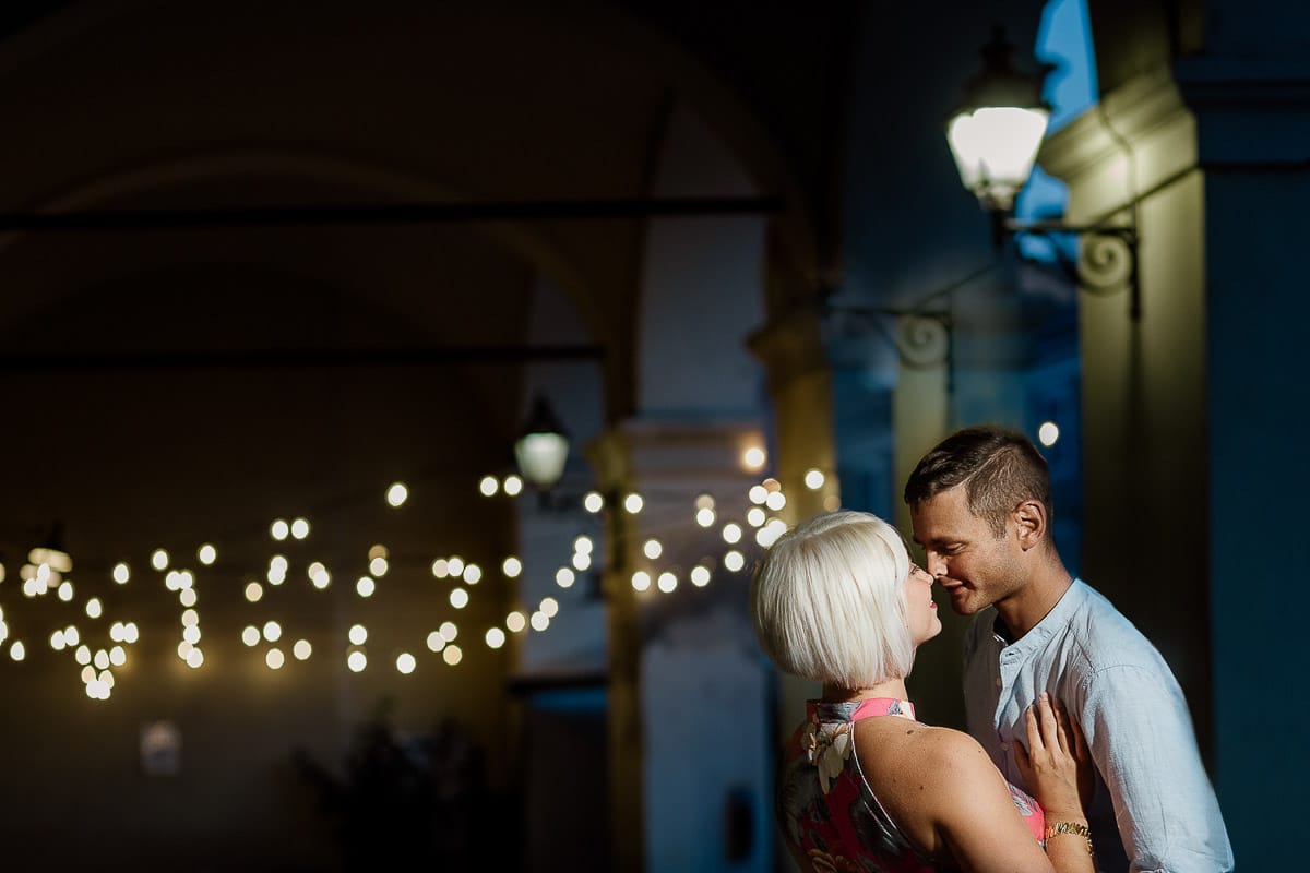 Prewedding da sogno a Nizza Monferrato nel centro storico. Fiammetta e Matteo davanti al bellissimo portone scolpito di un palazzo. storico. Flash off camera usato in modo sapiente illumina la coppia quando è ormai sera. Dietro di loro fili di luci che creano bokeh.