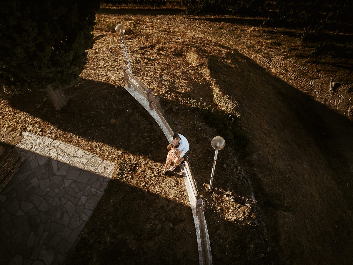 Prewedding da sogno a Nizza Monferrato intorno alla chiesa della Madonna della Neve. Matteo seduto su di una staccionata di legno abbraccia Fiammetta. Foto dal drone