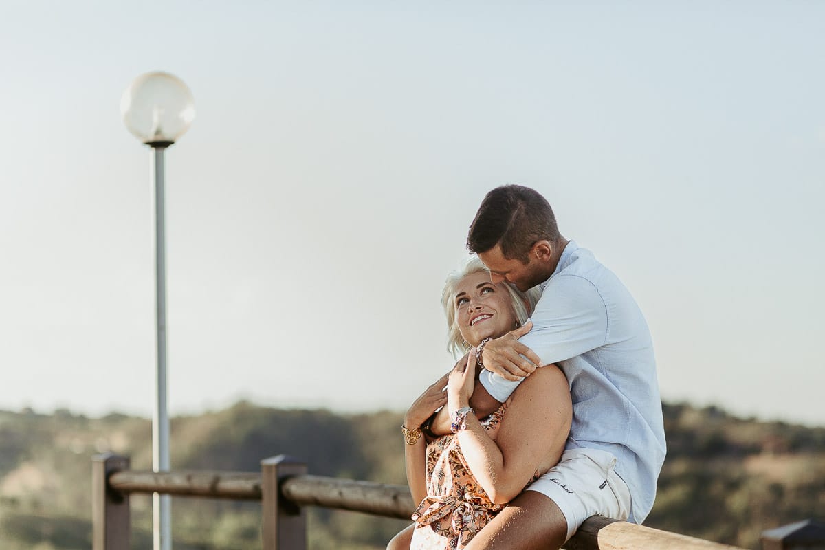 Prewedding da sogno a Nizza Monferrato intorno alla chiesa della Madonna della Neve. Matteo seduto su di una staccionata di legno abbraccia Fiammetta.