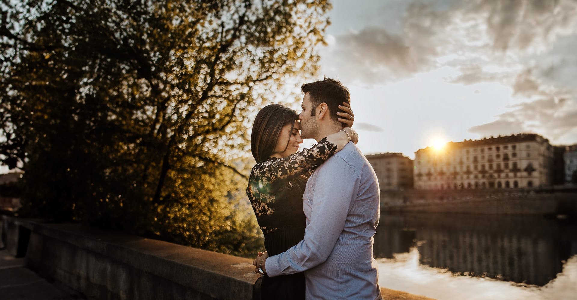 Prewedding a Torino. Raffaele bacia Alice sulla fronte davanti ad un meraviglioso tramonto illumina i palazzi storici e il fiume Po.