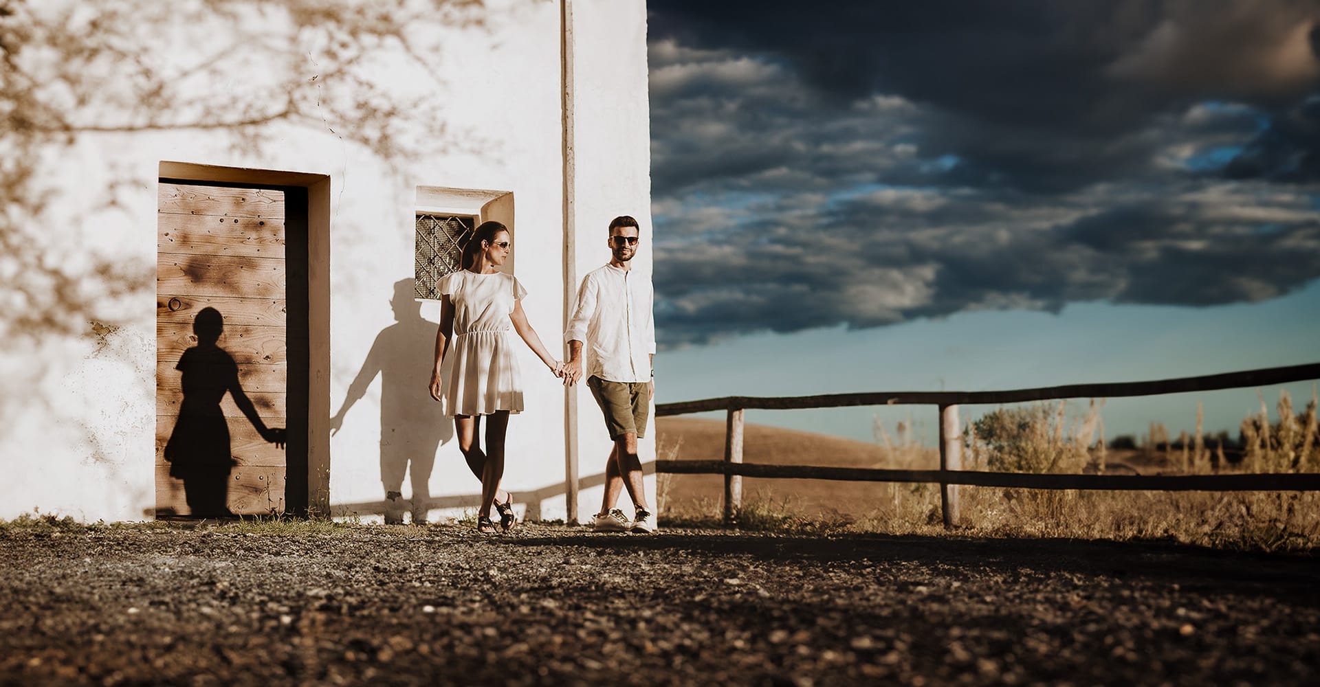 Prewedding spontaneo e poetico nel Monferrato, a Mombello di Torino. Federica e Riccardo si danno la mano davanti alla chiesa di san Lorenzo. Golden hour. Luce meravigliosa dopo la pioggia, con il cielo carico di nuvole molro suggestive.