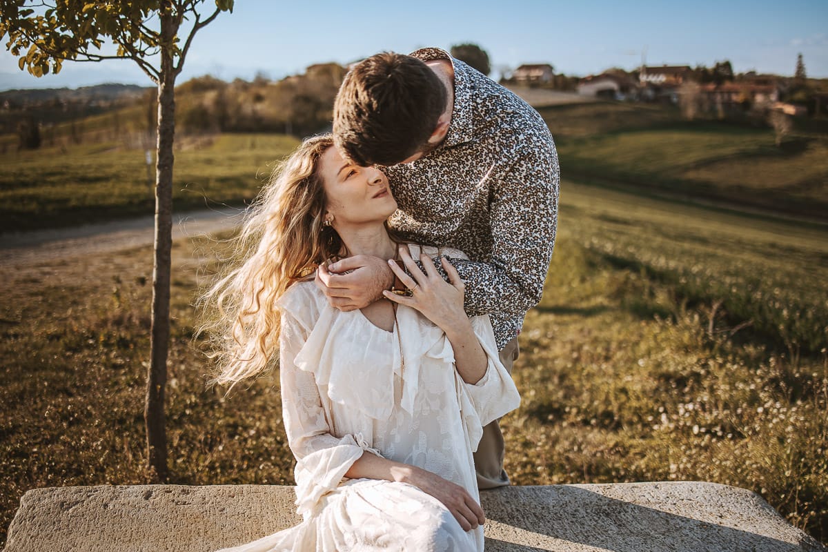 Mombello di Torino, Monferrato: Anita e Davide, raggianti di felicità, si scambiano un bacio davanti a una chiesetta romanica in un pittoresco pomeriggio primaverile. La foto cattura l'amore e l'emozione che precedono il loro matrimonio.