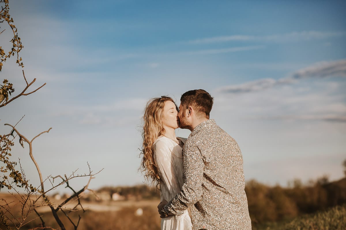 Mombello di Torino, Monferrato: Anita e Davide, raggianti di felicità, si scambiano un bacio davanti a una chiesetta romanica in un pittoresco pomeriggio primaverile. La foto cattura l'amore e l'emozione che precedono il loro matrimonio.