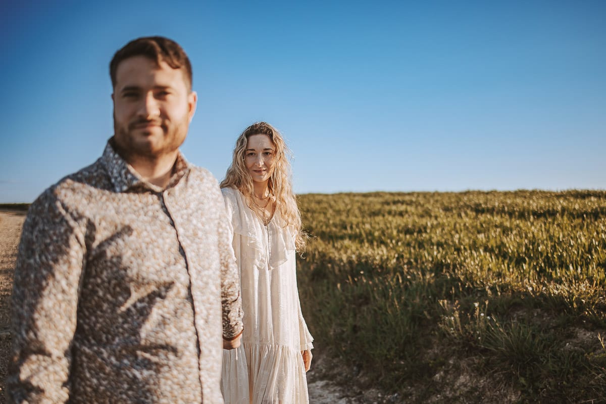 Anita e Davide, futuri sposi, si tengono per mano davanti a una chiesetta romanica a Mombello di Torino, baciati dal sole primaverile del Monferrato.