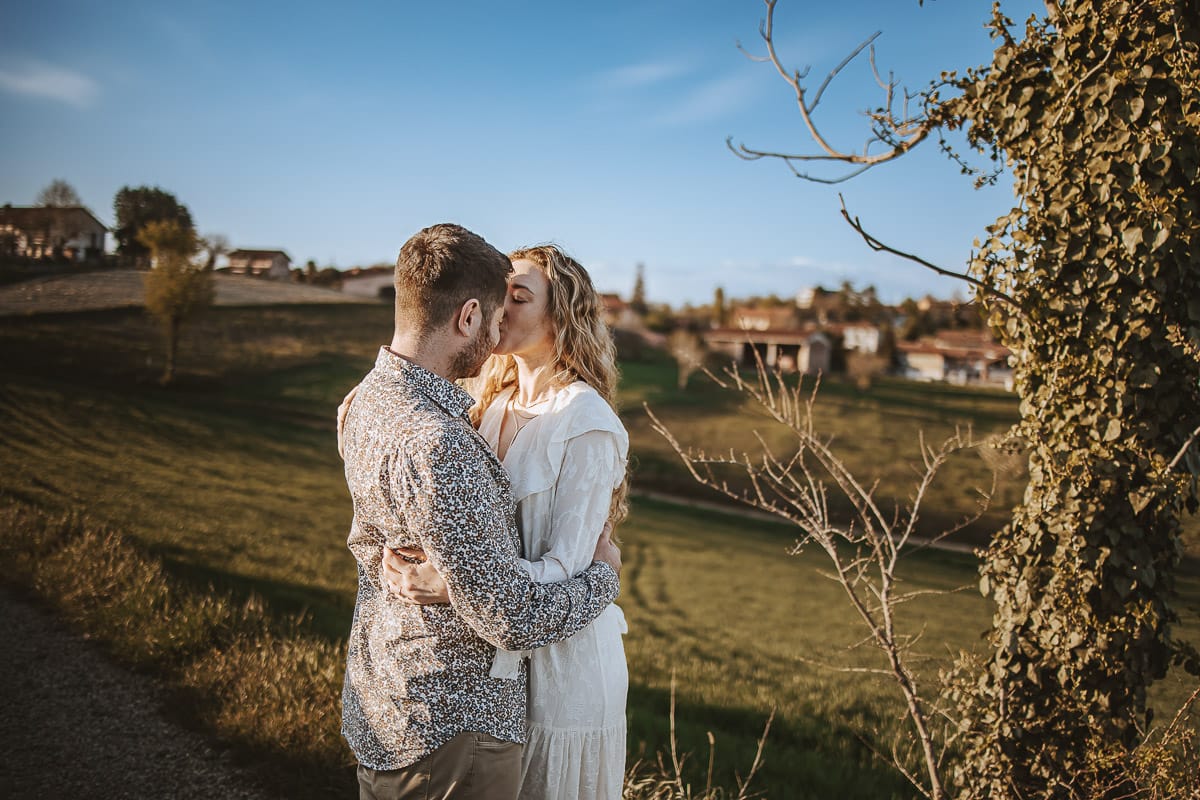 Mombello di Torino, Monferrato: Anita e Davide, raggianti di felicità, si scambiano un bacio davanti a una chiesetta romanica in un pittoresco pomeriggio primaverile. La foto cattura l'amore e l'emozione che precedono il loro matrimonio.