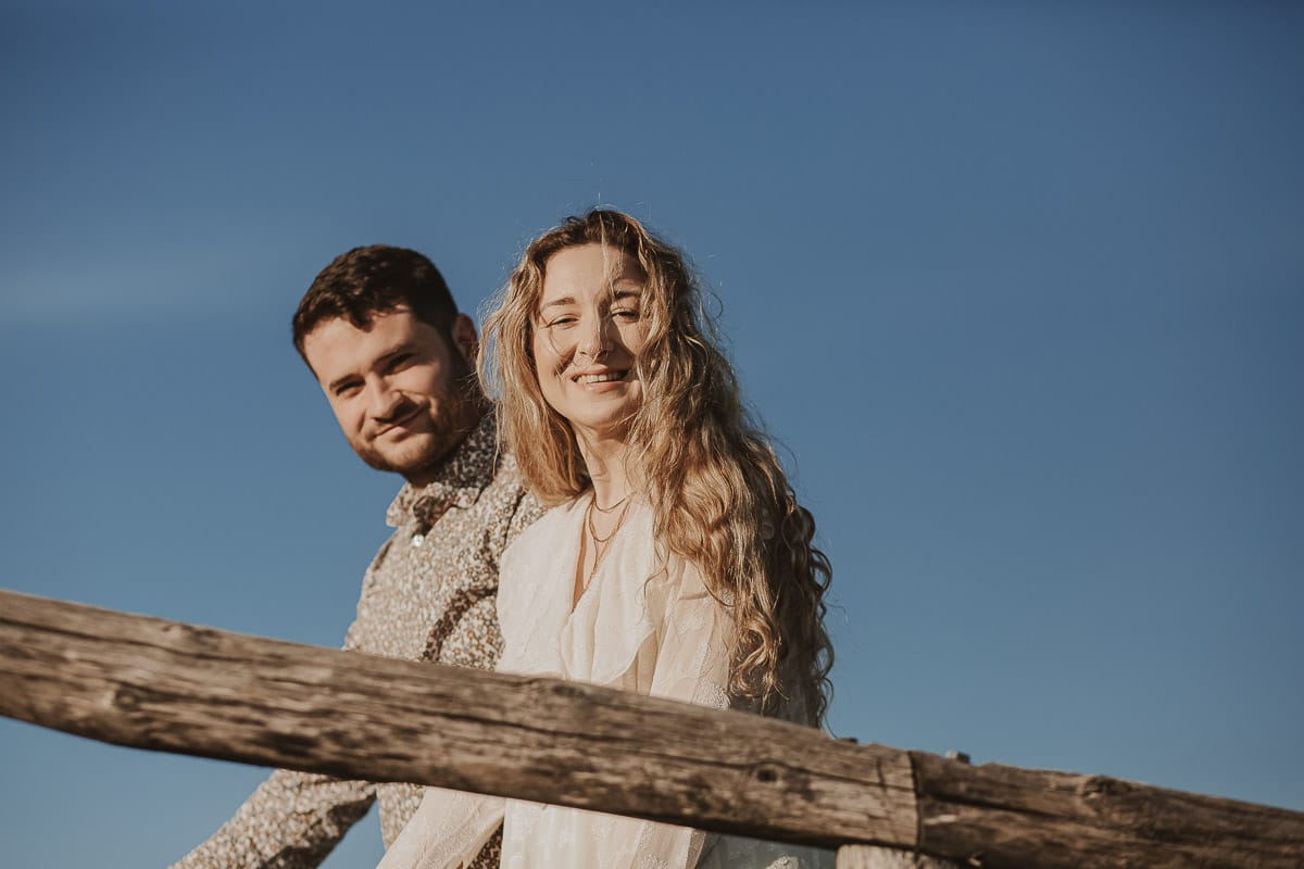 Anita e Davide, sposi novelli, si tengono per mano davanti a una chiesetta romanica a Mombello di Torino, immersi nella calda luce del sole primaverile del Monferrato.
