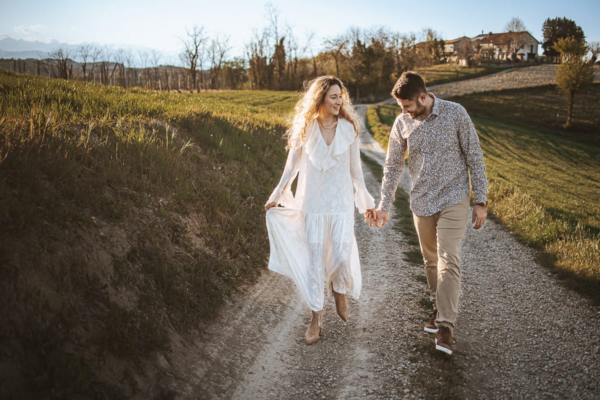 Anita e Davide, futuri sposi, si tengono per mano davanti a una chiesetta romanica a Mombello di Torino, baciati dal sole primaverile del Monferrato.