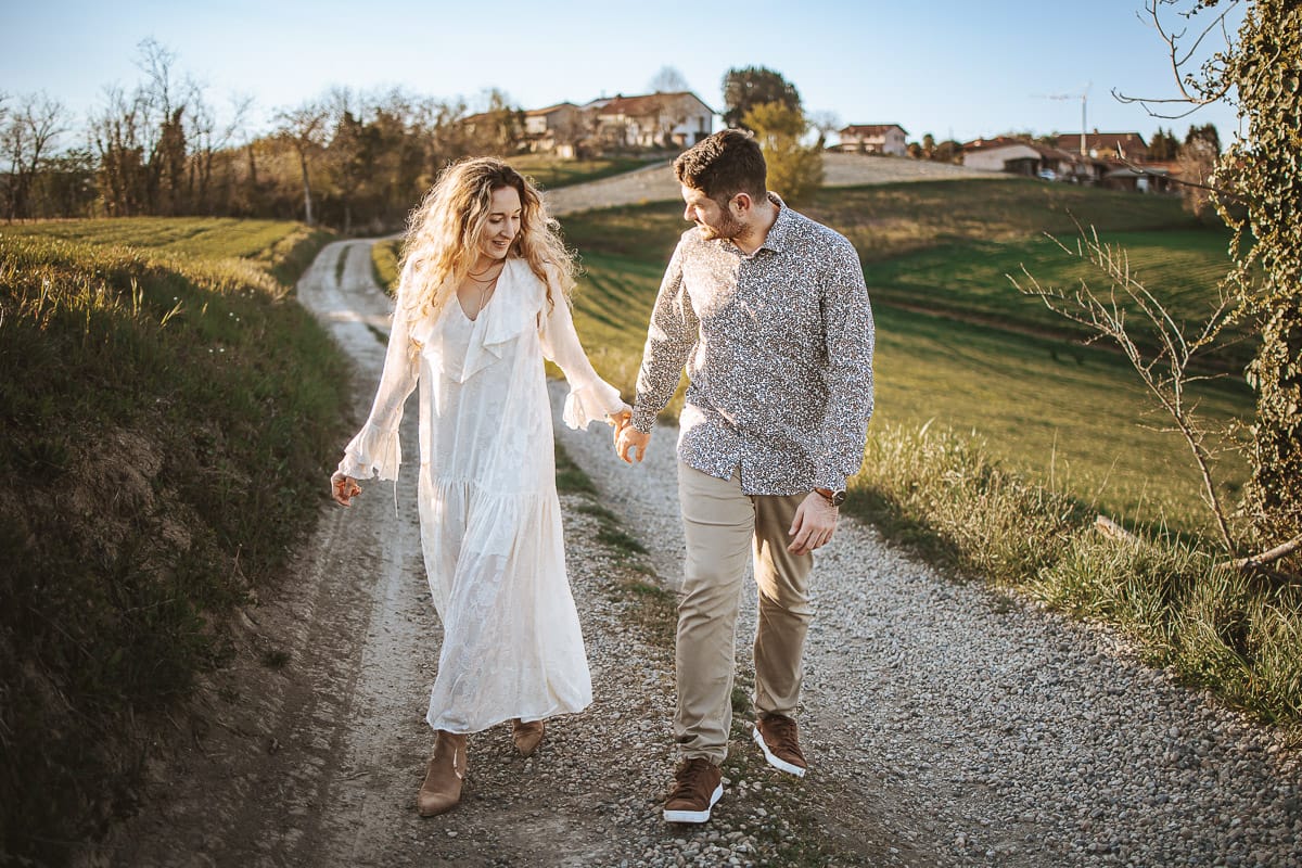 Anita e Davide, futuri sposi, si tengono per mano davanti a una chiesetta romanica a Mombello di Torino, baciati dal sole primaverile del Monferrato.