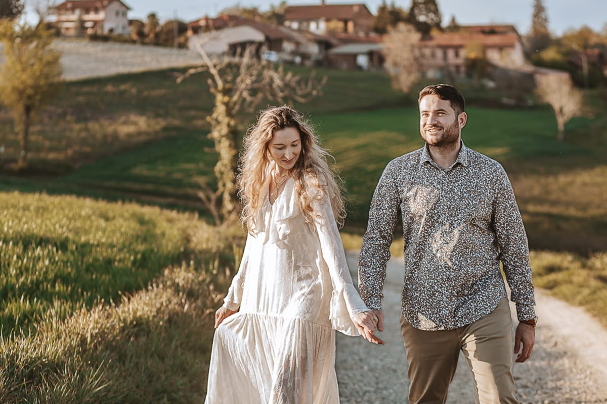 Anita e Davide, futuri sposi, si tengono per mano davanti a una chiesetta romanica a Mombello di Torino, baciati dal sole primaverile del Monferrato.