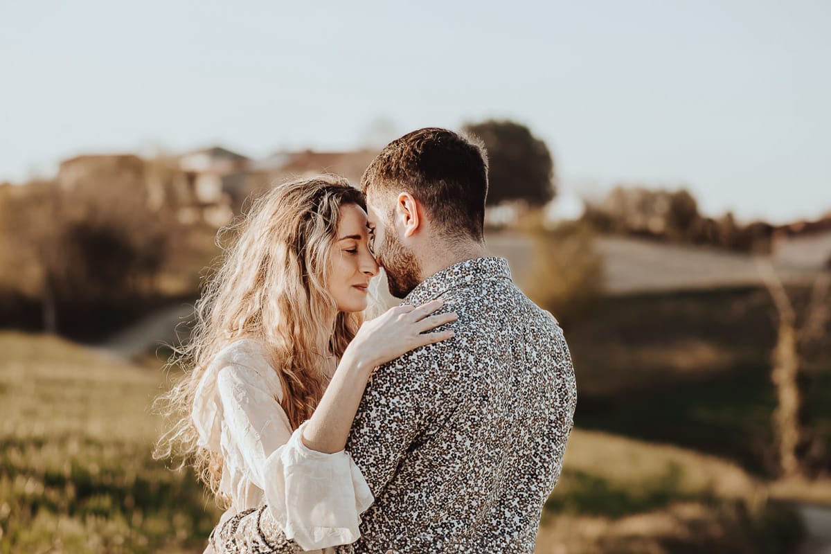 Mombello di Torino, Monferrato: Anita e Davide, raggianti di felicità, si scambiano un bacio davanti a una chiesetta romanica in un pittoresco pomeriggio primaverile. La foto cattura l'amore e l'emozione che precedono il loro matrimonio.