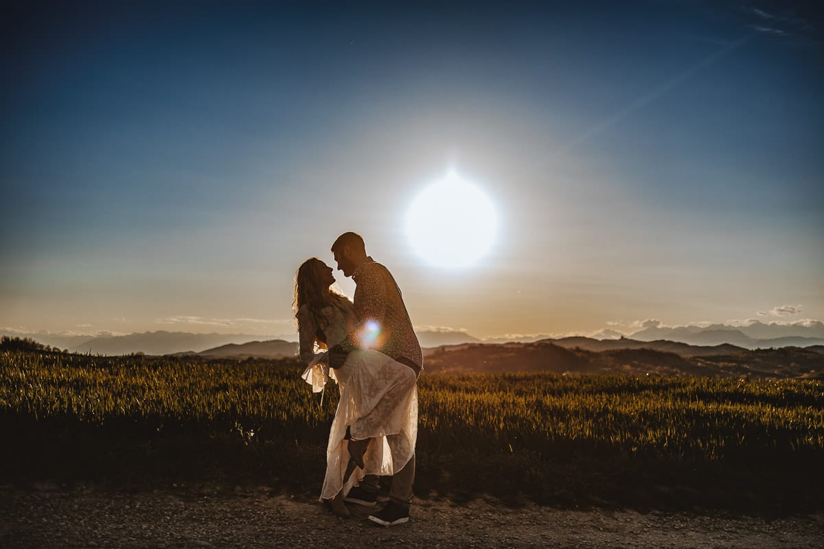 Mombello di Torino, Monferrato: Anita e Davide, futuri sposi, si scambiano un bacio davanti alla chiesetta di San Lorenzo. La foto in controluce crea un'atmosfera magica e romantica, simbolo del loro amore e della loro promessa di vita insieme.