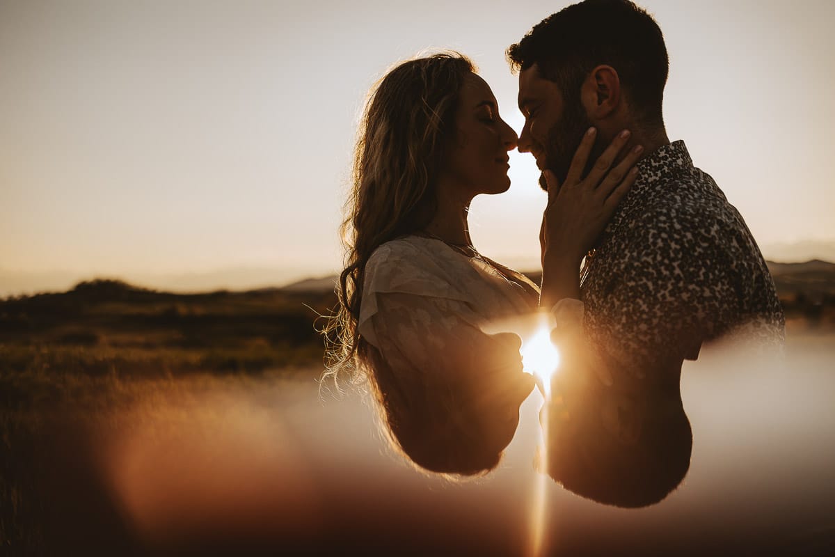 Mombello di Torino, Monferrato: Anita e Davide, futuri sposi, si scambiano un bacio davanti alla chiesetta di San Lorenzo. La foto in controluce crea un'atmosfera magica e romantica, simbolo del loro amore e della loro promessa di vita insieme.