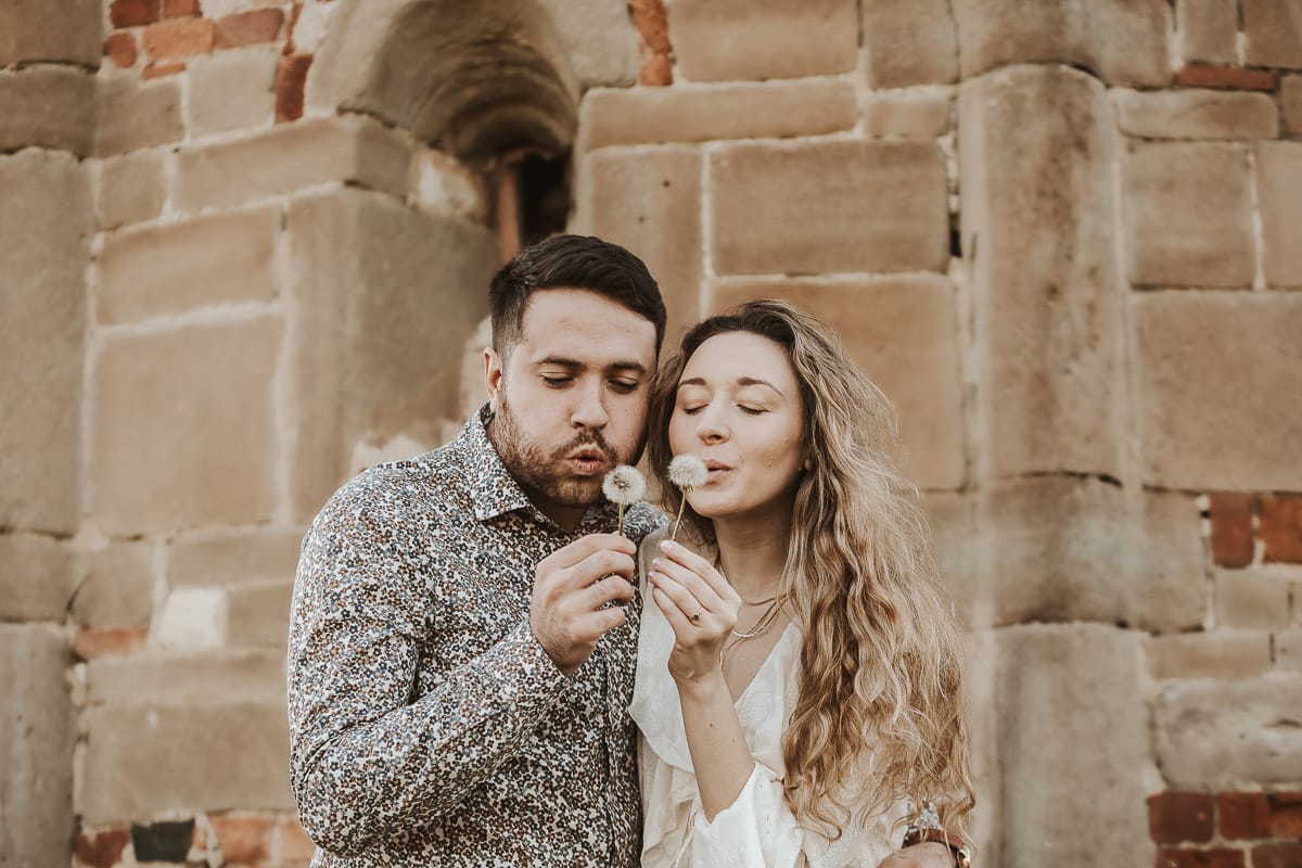 Un ritratto romantico di Anita e Davide, futuri sposi, in una soleggiata giornata primaverile. La coppia si trova di fronte a una chiesetta romanica a Mombello di Torino, nel cuore del Monferrato. La coppia soffia un soffione