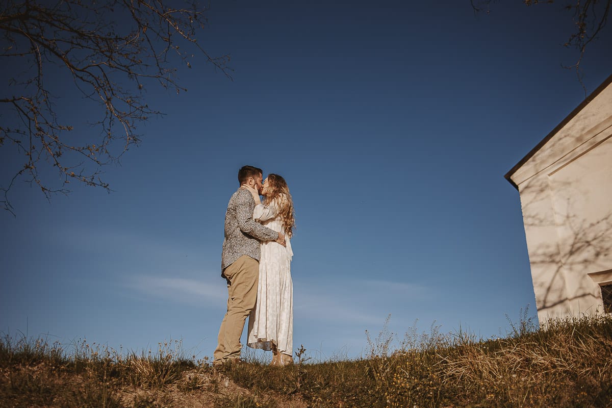 Mombello di Torino, Monferrato: Anita e Davide, raggianti di felicità, si scambiano un bacio davanti a una chiesetta romanica in un pittoresco pomeriggio primaverile. La foto cattura l'amore e l'emozione che precedono il loro matrimonio.