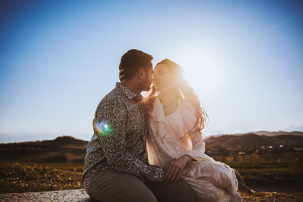 Mombello di Torino, Monferrato: Anita e Davide, raggianti di felicità, si scambiano un bacio davanti a una chiesetta romanica in un pittoresco pomeriggio primaverile. La foto cattura l'amore e l'emozione che precedono il loro matrimonio.