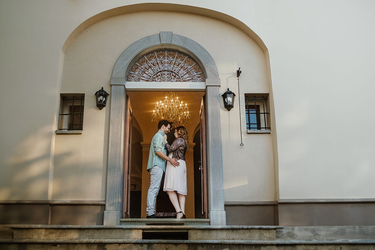 Fotografo matrimonio Rivalba. Villa Ala. Prewedding di Giorgia e Marco. Golden Hour. La coppia è fronte fronte davanti ad uno dei portoni della villa. Dietro di loro il grande lampadario a gocce.