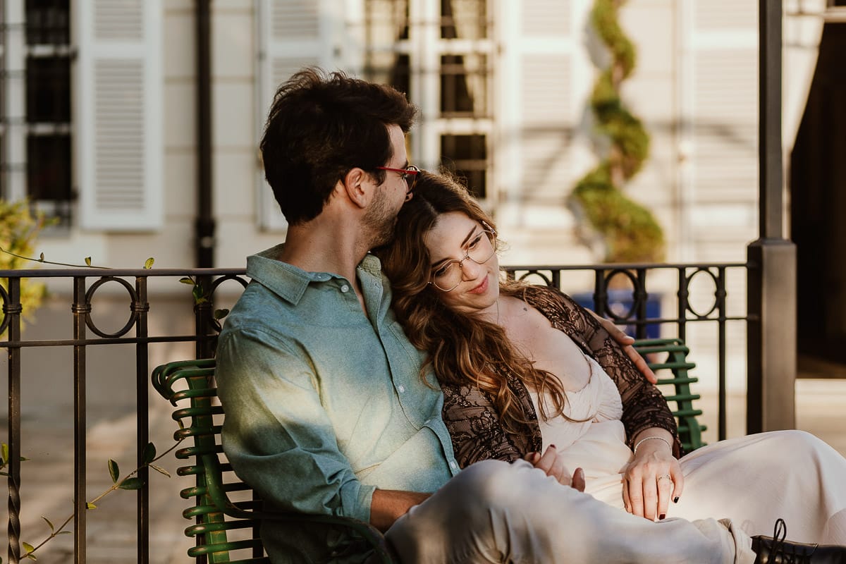Fotografo matrimonio Rivalba. Villa Ala. Prewedding di Giorgia e Marco. Golden Hour. La coppia è seduti su di una panchina di ferro battuto, davanti alla villa sotto un gazebo in ferro battuto. Giorgia appoggia dolcemente la testa sulla spalla di Marco