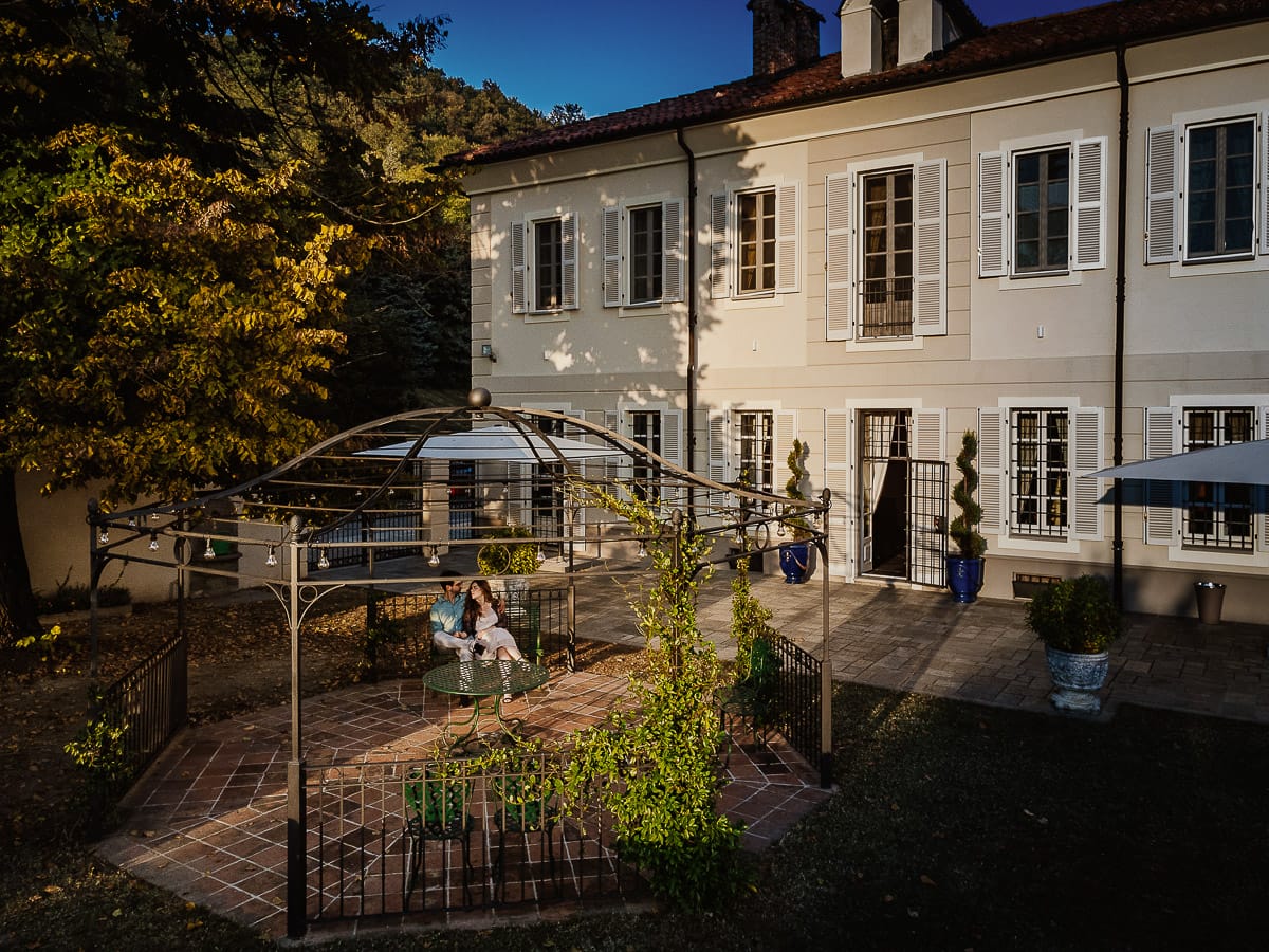 Fotografo matrimonio Rivalba. Villa Ala. Prewedding di Giorgia e Marco. Golden Hour. La coppia è seduti su di una panchina di ferro battuto, davanti alla villa sotto un gazebo in ferro battuto.Foto dal drone.