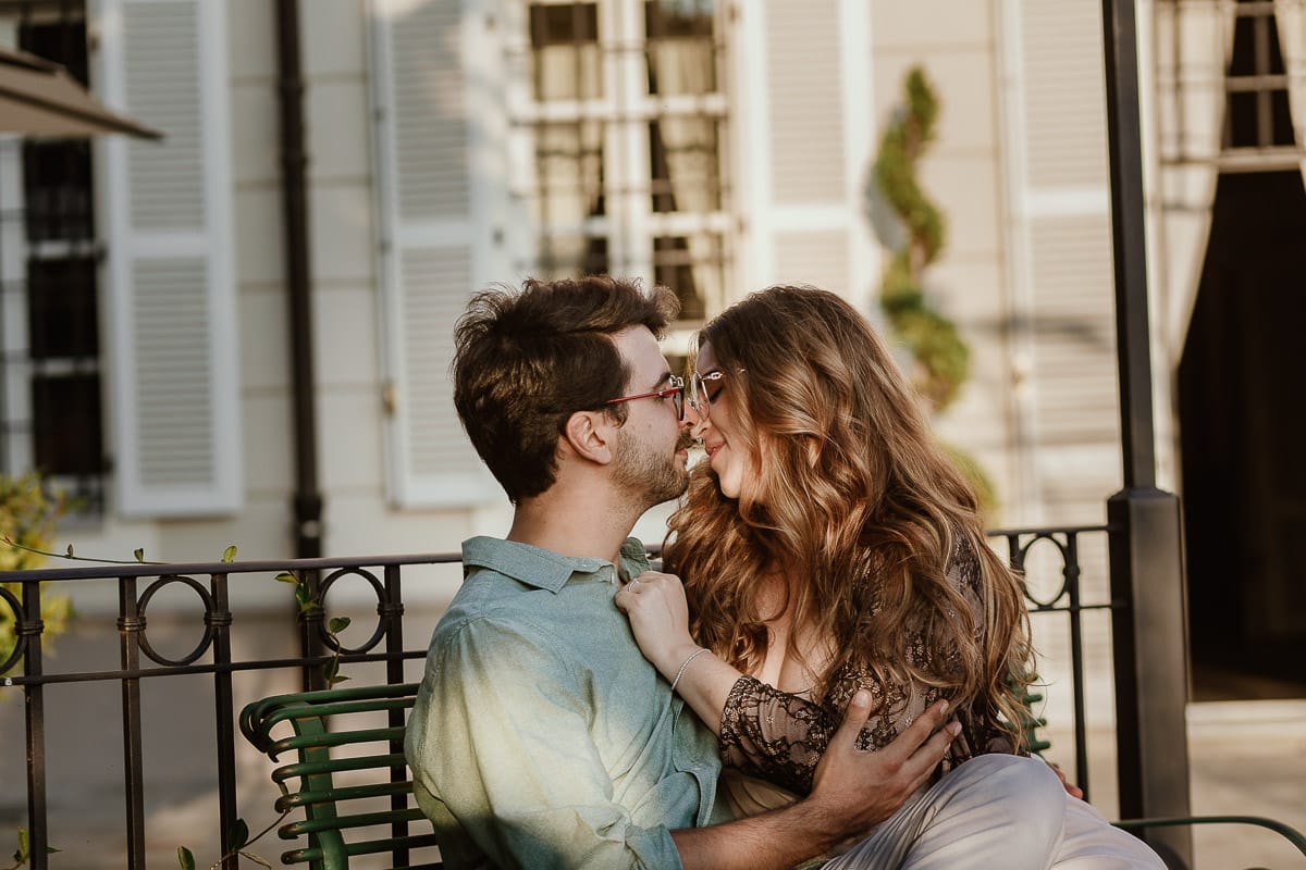 Fotografo matrimonio Rivalba. Villa Ala. Prewedding di Giorgia e Marco. Golden Hour. La coppia è seduti su di una panchina di ferro battuto, davanti alla villa sotto un gazebo in ferro battuto. Marco bacia la fronte di Giorgia