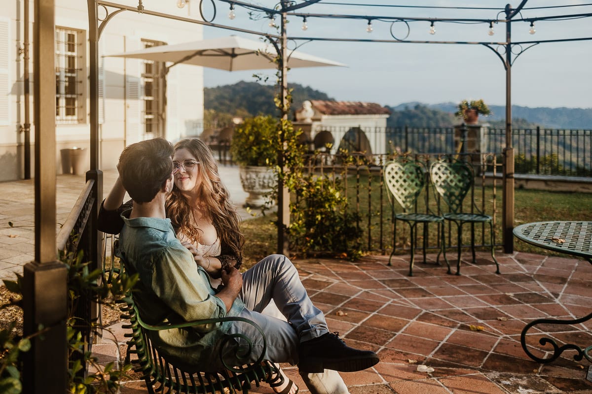 Fotografo matrimonio Rivalba. Villa Ala. Prewedding di Giorgia e Marco. Golden Hour. La coppia è seduti su di una panchina di ferro battuto, davanti alla villa sotto un gazebo in ferro battuto. la coppia si guarda teneramente