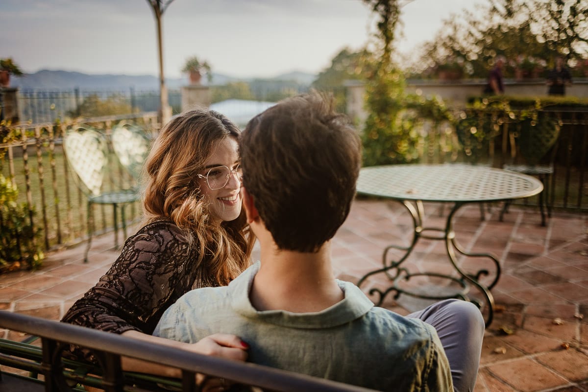 Fotografo matrimonio Rivalba. Villa Ala. Prewedding di Giorgia e Marco. Golden Hour. La coppia è seduti su di una panchina di ferro battuto, davanti alla villa sotto un gazebo in ferro battuto. Ritratto ravvicinato. Giorgia guarda Marco teneramente