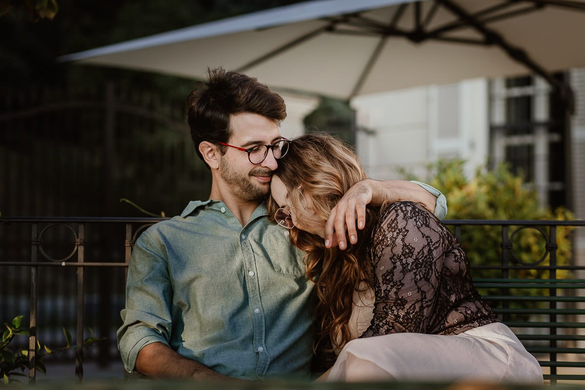 Fotografo matrimonio Rivalba. Villa Ala. Prewedding di Giorgia e Marco. Golden Hour. La coppia è seduti su di una panchina di ferro battuto, davanti alla villa sotto un gazebo in ferro battuto. Marco abbraccia teneramente Giorgia