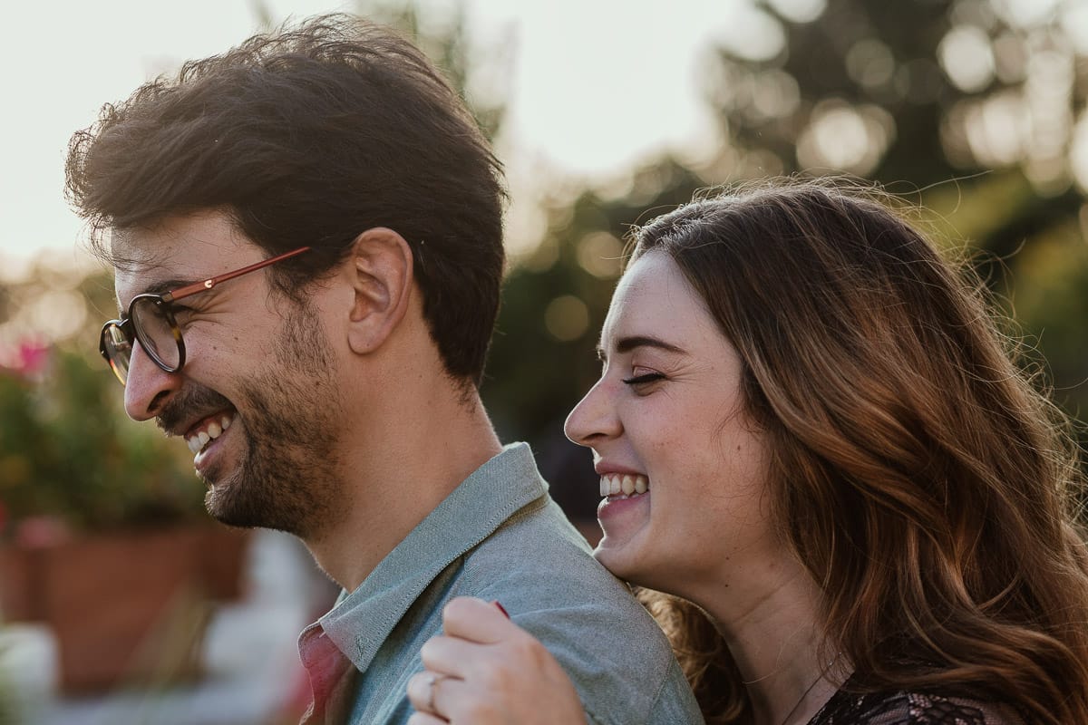 Fotografo matrimonio Rivalba. Villa Ala. Prewedding di Giorgia e Marco. Golden Hour. La coppia è seduti su di una panchina di ferro battuto, davanti alla villa sotto un gazebo in ferro battuto. Ritratto. la coppia ride