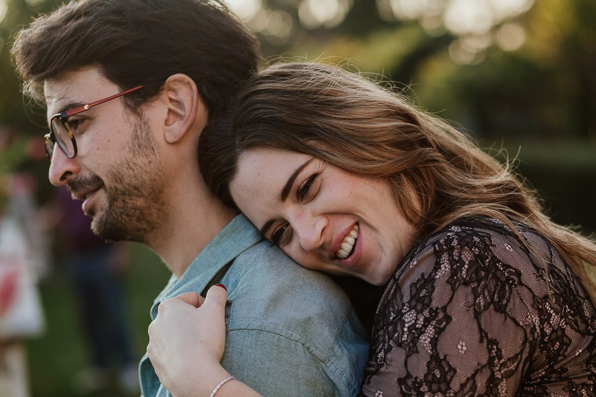 Fotografo matrimonio Rivalba. Villa Ala. Prewedding di Giorgia e Marco. Golden Hour. La coppia è seduti su di una panchina di ferro battuto, davanti alla villa sotto un gazebo in ferro battuto. Ritratto. Giorgia è dietro Marco e si appoggia teneramente a lui.