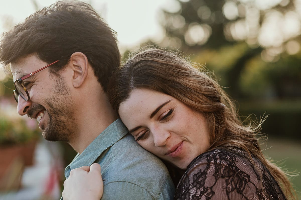 Fotografo matrimonio Rivalba. Villa Ala. Prewedding di Giorgia e Marco. Golden Hour. La coppia è seduti su di una panchina di ferro battuto, davanti alla villa sotto un gazebo in ferro battuto. Ritratto. Giorgia è dietro Marco e si appoggia teneramente a lui.