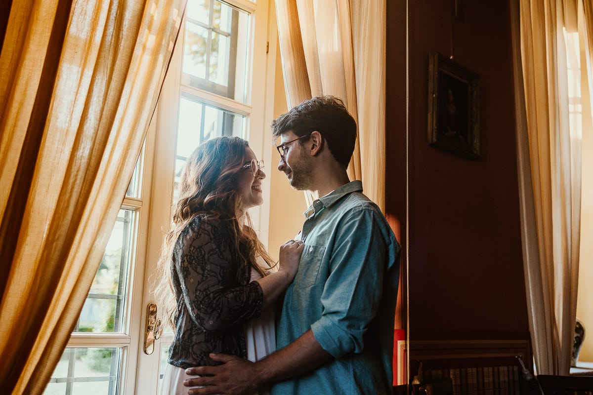 Fotografo matrimonio Rivalba. Villa Ala. Prewedding di Giorgia e Marco. Golden Hour. Ritratto vicino ad una finestra tra i tendaggi gialli.