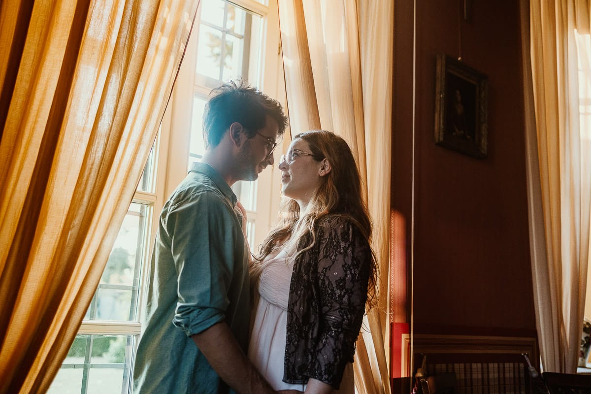 Fotografo matrimonio Rivalba. Villa Ala. Prewedding di Giorgia e Marco. Golden Hour. Ritratto vicino ad una finestra tra i tendaggi gialli.