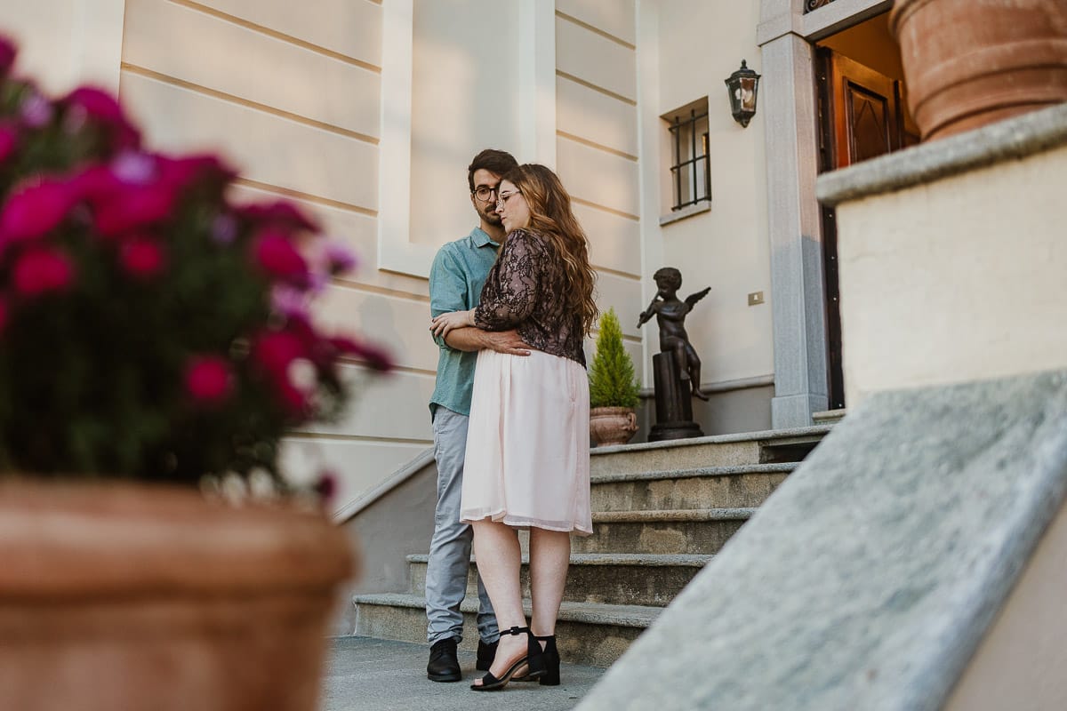 Fotografo matrimonio Rivalba. Villa Ala. Prewedding di Giorgia e Marco. Golden Hour. La coppia esce dalla villa. Ritratto ripreso attraverso un vaso di fiori.