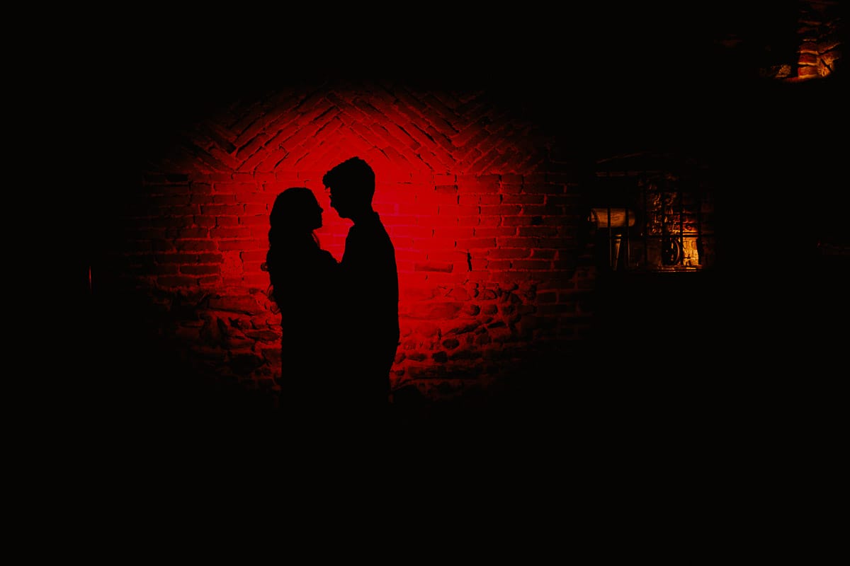 Fotografo matrimonio Rivalba. Villa Ala. Prewedding di Giorgia e Marco. Foto nella cantina della villa. Silhouette. Flash esterno puntato contro il muro di mattoni con gelatina rossa.