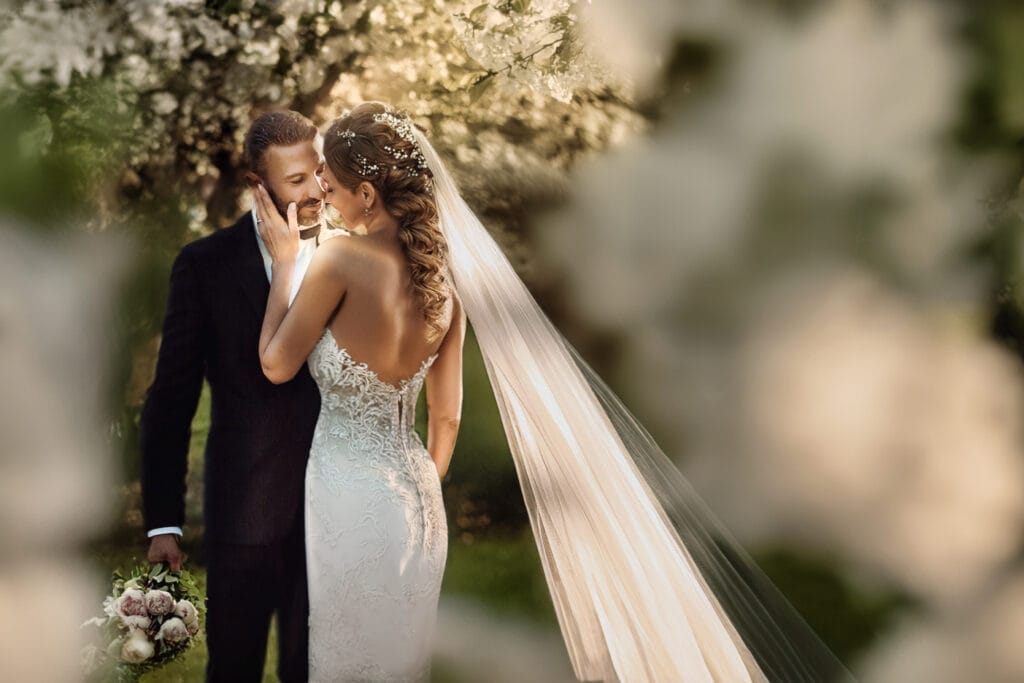 Tendenze matrimoni 2025. Sposi al tramonto in un giardino con alberi in fiori. Bouquet naturale di peonie