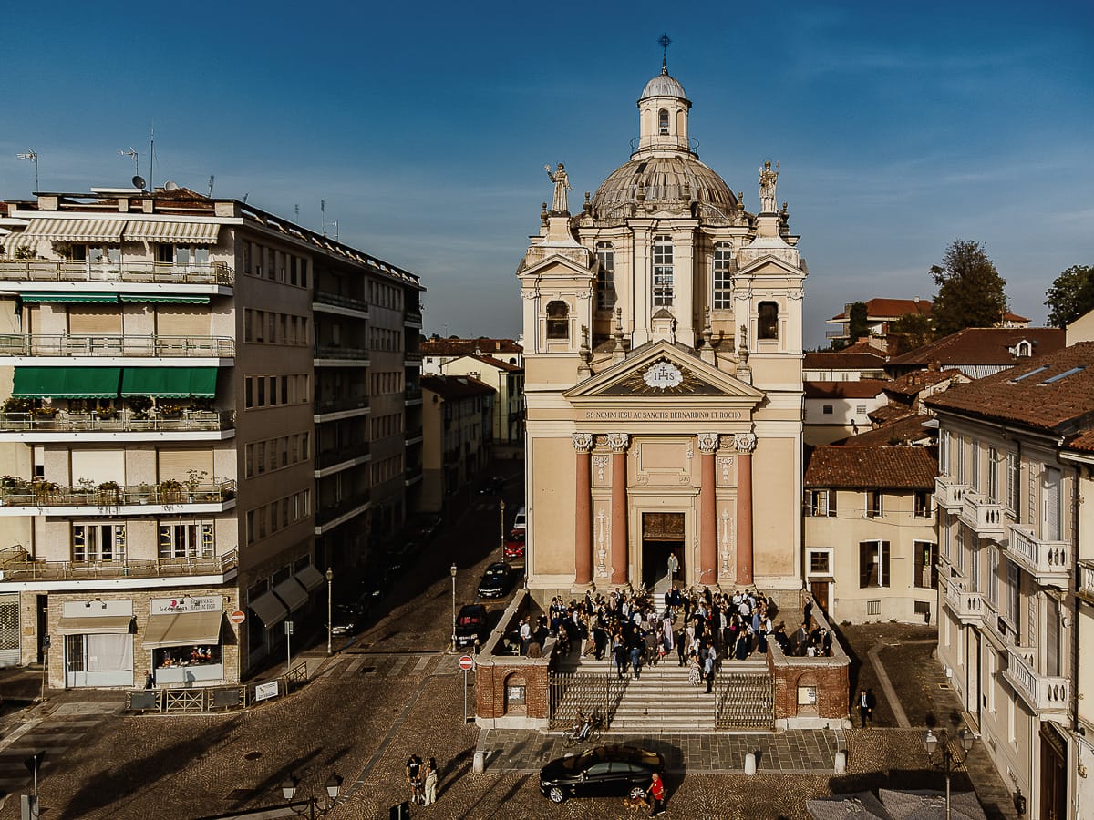 Fotografo matrimonio Torino. Matrimonio eco-consapevole a Cascina Ranverso. Cerimonia a Chieri nella chiesa dei Santi Bernardino e Rocco. Uscita. gli invitati aspettano fuori sul sagrato della chiesa. Foto panoramica dal drone.